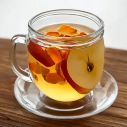 Glass mug with clear apple peel tea and full apple slice on wooden table
